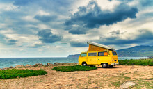 Yellow Camper Van Standing In Front Of The Sea On A Cliff With Dramatic Sky - Travel Concept.