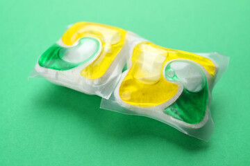 Two dishwasher detergent pods on green background, closeup