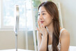 © KMPZZZ - Fresh healthy skin, beautiful smile of asian young woman, girl looking at mirror, applying moisturizer on her face, putting cream treatment before make up cosmetic routine at home. Facial Beauty.