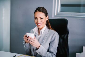 Wall Mural - A businesswoman taking a break with cup of coffee at modern office and smiling at the camera.