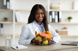 © Prostock-studio - Portrait of black female nutritionist sitting at worplace with bowl of fresh fruits, working at weight loss clinic