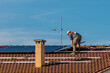 A technician lays the solar panels of a photovoltaic system on top of a red-tiled roof
