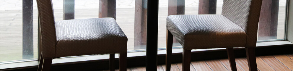 Two chairs and black metal table base near dirty ceiling to floor window with wood grille panels wall outside as decor at daytime