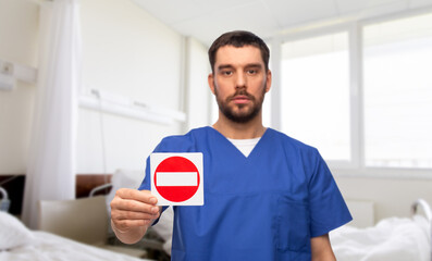 Wall Mural - healthcare, profession and medicine concept - male doctor in blue uniform showing stop sign over hospital ward background