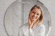 © Prostock-studio - Pretty caucasian woman looking at mirror, touching her skin and smiling at her reflection, standing in bathroom