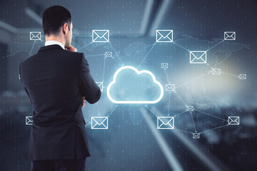 Poster - Attractive young european businessman with glowing cloud email netwrok hologram standing in blurry office interior. Innovation, online communication and computing concept. Double exposure.
