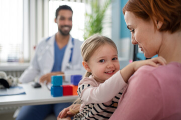 Wall Mural - little girl with her mother at doctor's office on consultation, looking at camera.