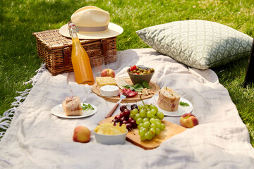 Wall Mural - leisure and eating concept - close up of food, drinks and picnic basket on blanket on grass at summer park