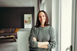 Portrait of smiling woman with arms crossed leaning by window at home