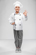 cooking, culinary and profession concept - happy smiling little girl in chef's toque and jacket showing ok gesture over grey background