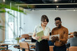 © Tijana - Happy Businesswoman and Businessman Using Digital Tablet Together at Work. Two smiling colleagues analyzing business report on a tablet while unrecognizable multi-ethnic team working at desk.