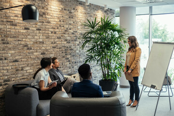 Wall Mural - Smiling Business Woman Presenting Business Strategy on a White Board at Work. 

Happy multiracial group of business peoples in a casual meeting at their company listening to female colleague speech.