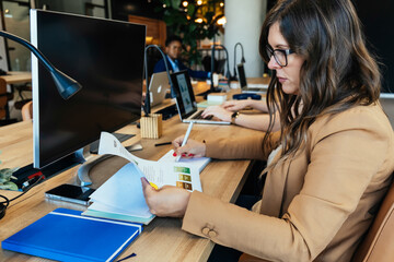 Wall Mural - Serious Business Woman Analyzing Business Graphs at Work. 
Beautiful businesswoman reading business reports while sitting in modern open plan office with multi-ethnic team.