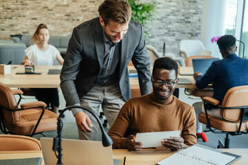 Two Happy Businessman Using Digital Tablet at Work. 

Happy boss and his employee looking at business report on a tablet while multi-ethnic team of business people working in background.