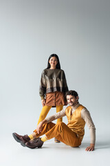 Wall Mural - smiling man in yellow trousers sitting near asian woman in leather jacket on grey