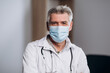 © Owl-vision-studio - Close up portrait of male doctor in medical mask posing for camera. Family therapist sitting at workplace.
