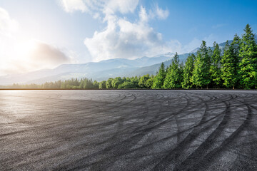 Empty asphalt road and green forest with mountain scenery at sunrise