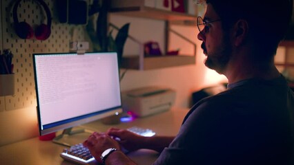 young adult man working on the computer at home, man is typing on keyboard at night, programmer coding from home office