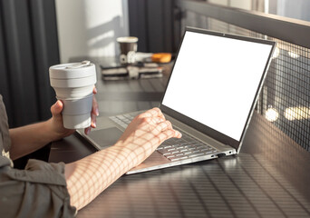 Poster - Female hands holding eco cup and working on laptop. Businesswoman sitting in cafe and using computer mockup for work, study, social communication. High quality photo