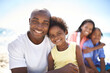 © Tasneem H/peopleimages.com - Making the most of the sun together. A daughter and father enjoying a day on the beach with mom and brother in the background.