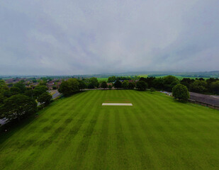 Poster - A sized piece of green land surrounded with dense trees near the residential area on a gloomy day