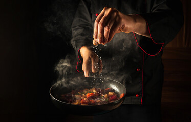 cooking fresh vegetables. the chef adds salt to a steaming hot pan. grande cuisine idea for a hotel 