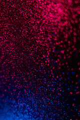 Color bokeh glow. Glitter background. Wet asphalt reflection. Defocused neon blue red light shiny sparkles round flecks texture on dark black abstract overlay.