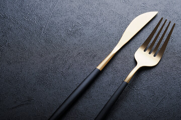 Wall Mural - Gold spoon, fork, knife and clean empty black plate. Set of stylish black and gold cutlery on black background. Fashionable and luxury eating. Top view. Copy space for your text.