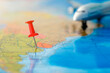 a close-up of a pushpin stuck in a map, with an airplane in the background. The concept is travel, air travel to anywhere in the world. Horizontal photo.