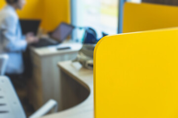 View of modern office space interior with desks in yellow tones with workers, employee with a laptop on a cozy workplace in the background, it-company open space with tables, chairs and rooms