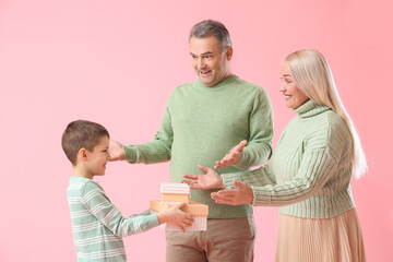 Little boy giving presents to his grandparents in warm sweaters on pink background
