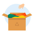 Cardboard box with old clothes for recycling and donating. The hand throws the clothes into the box