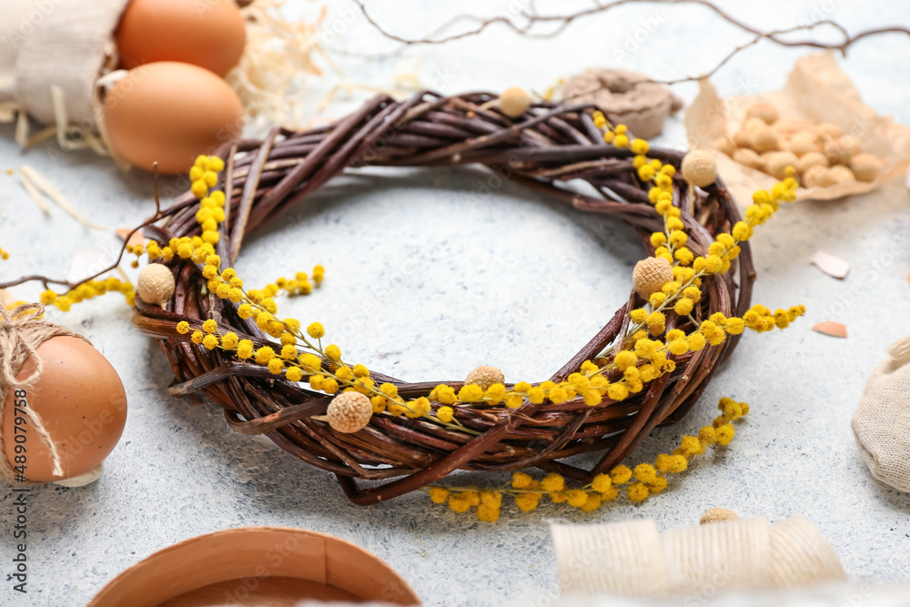 Easter wreath with floral decor and eggs on light background, closeup