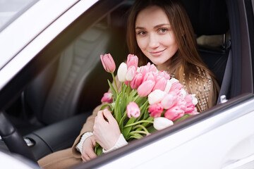 Beautiful girl with tulip flowers in her hands in the car  