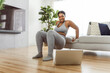 © Louis-Paul Photo - African american woman working out in home livingroom gym with laptop