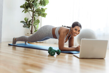 Wall Mural - African american woman working out abdo in home livingroom gym with laptop