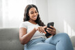 © Louis-Paul Photo - Attractive young African woman sitting on the couch at home with cellphone