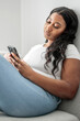 © Louis-Paul Photo - Attractive young African woman sitting on the couch at home with cellphone