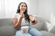 © Louis-Paul Photo - Attractive young African woman sitting on the couch at home eating popcorn