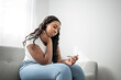 © Louis-Paul Photo - Unhappy black woman looking at pregnancy test upset by result sitting on couch