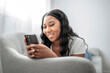 © Louis-Paul Photo - Attractive young African woman sitting on the couch at home with cellphone