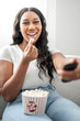 © Louis-Paul Photo - Attractive young African woman sitting on the couch at home eating popcorn