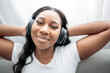 © Louis-Paul Photo - Attractive young African woman sitting on the couch at home listening music with headphone