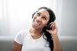 © Louis-Paul Photo - Attractive young African woman sitting on the couch at home listening music with headphone