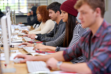 Poster - Focussed on their studies. Shot of students working on computers in a university library.