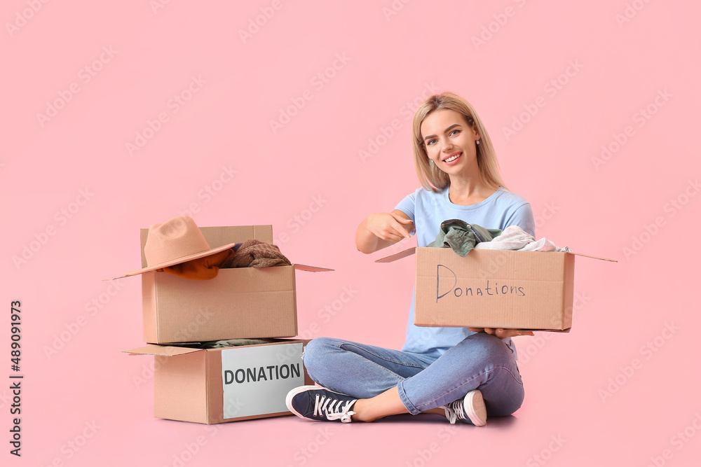 Young woman and boxes with clothes for donation on pink background