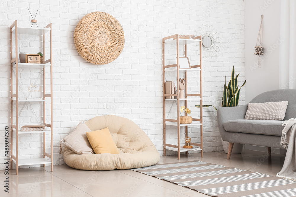 Interior of light room with comfortable pouf and shelf units near white brick wall