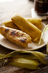 Wall Mural - Humitas are savory steamed fresh corn cakes, a traditional Ecuadorian appetizer. It’s accompanied by coffee, on a wooden background. 