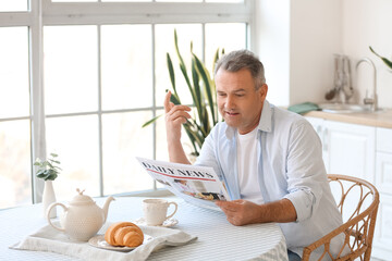 Wall Mural - Senior man reading newspaper at table in kitchen