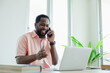 © eakgrungenerd - Black male african american receiving talking mobile phone and working research business with laptop at office table.